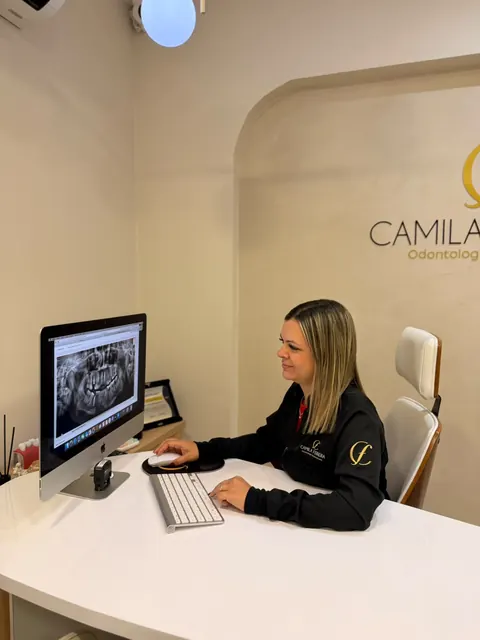 Dra. Camila Ferreira no consultório, analisando uma radiografia panorâmica no computador