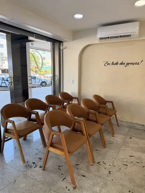 Recepção renovada da clínica, com poltronas de couro caramelo, vitrine de vidro e a frase Em tudo dai graças na parede