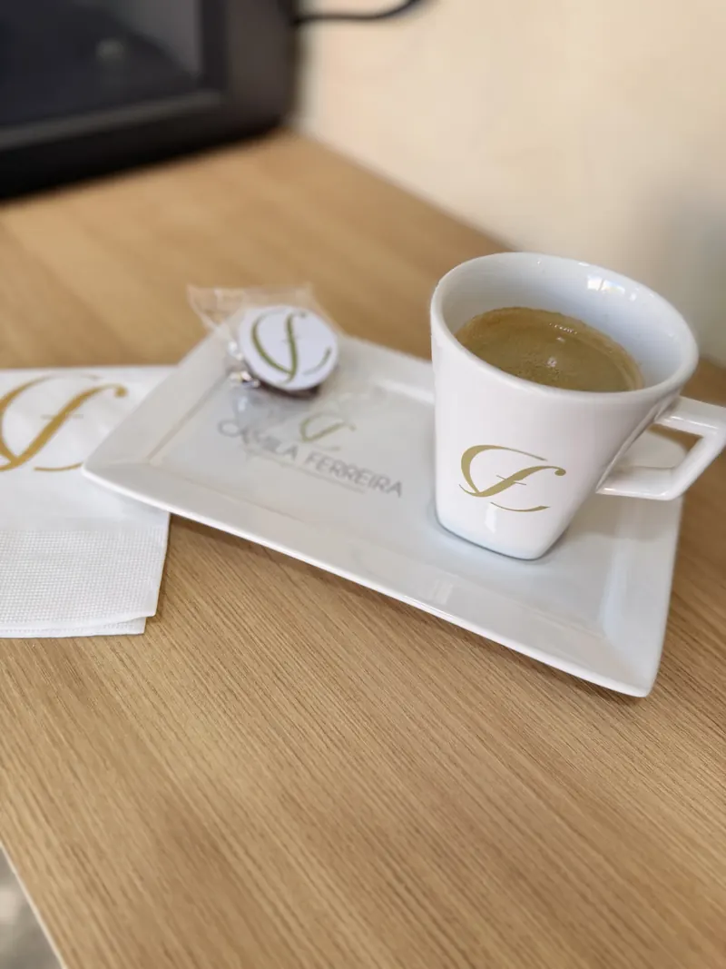 Xícara de café com a marca da clínica Camila Ferreira, servida na recepção com um chocolate